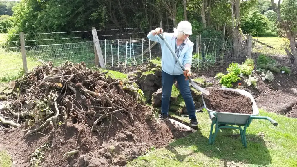 building a hugelkultur bed with mound in the background being covered with topsoil.