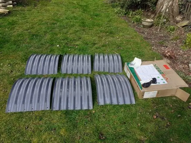 Circular steel bed unpacked from box still in pieces. Laid out on lawn waiting to be assembled