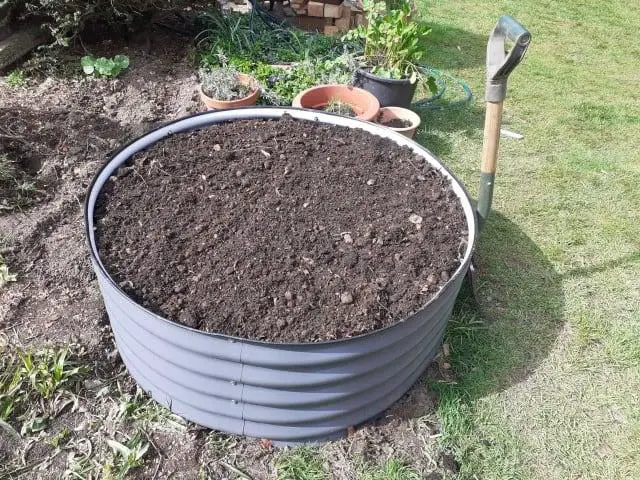 round raised garden bed recently filled with fresh soil. Spade leaning against the bed